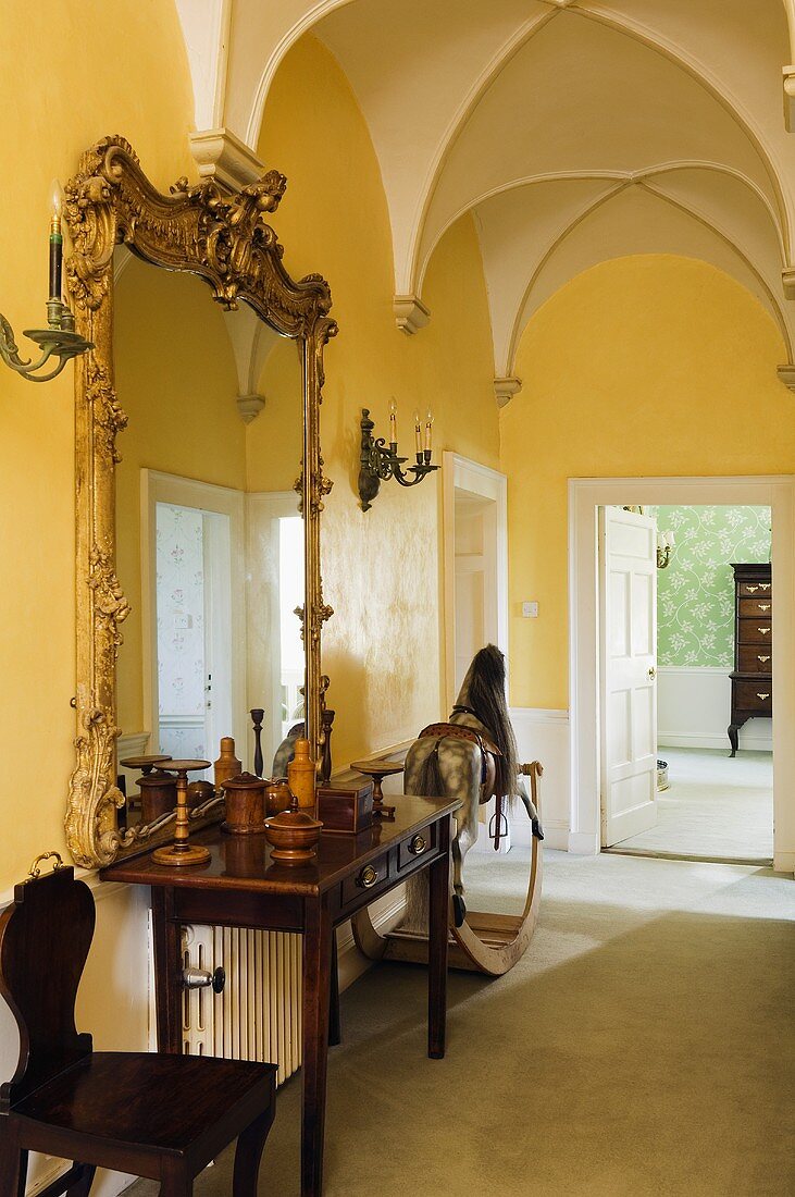 Gelber Flur mit Kreuzgratgewölbe und barockem Spiegel über Wandtisch und Blick auf offene Tür