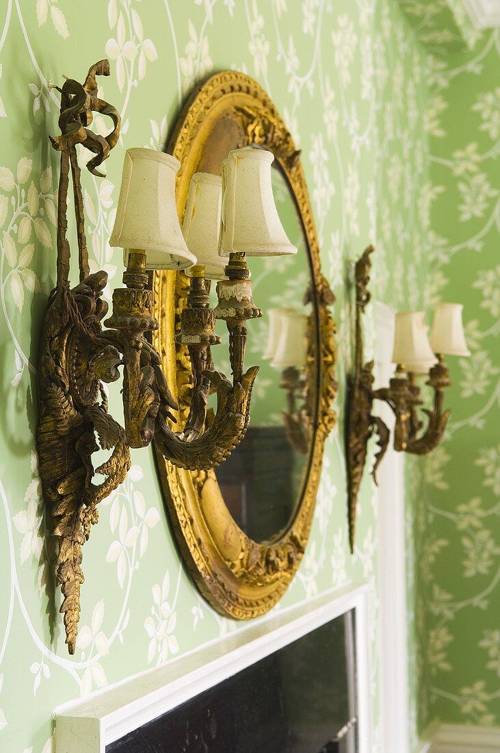 Lampen und Spiegel mit Goldrahmen an Wand mit floralem Tapetenmuster