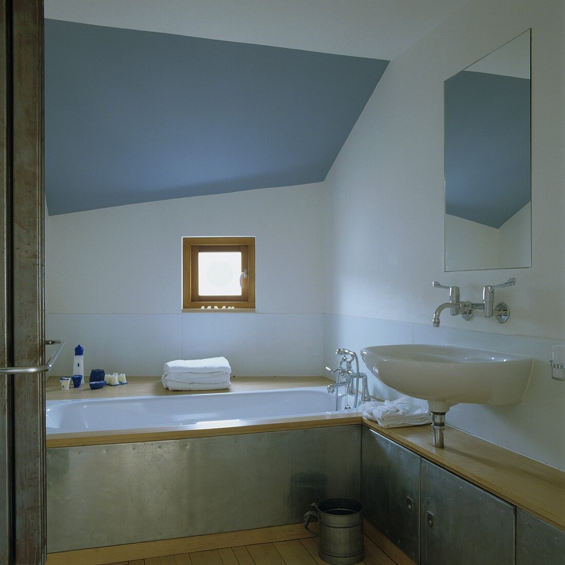 An attic bathroom with a blue ceiling - a wash basin and a built-in bathroom with circumferential metal cladding