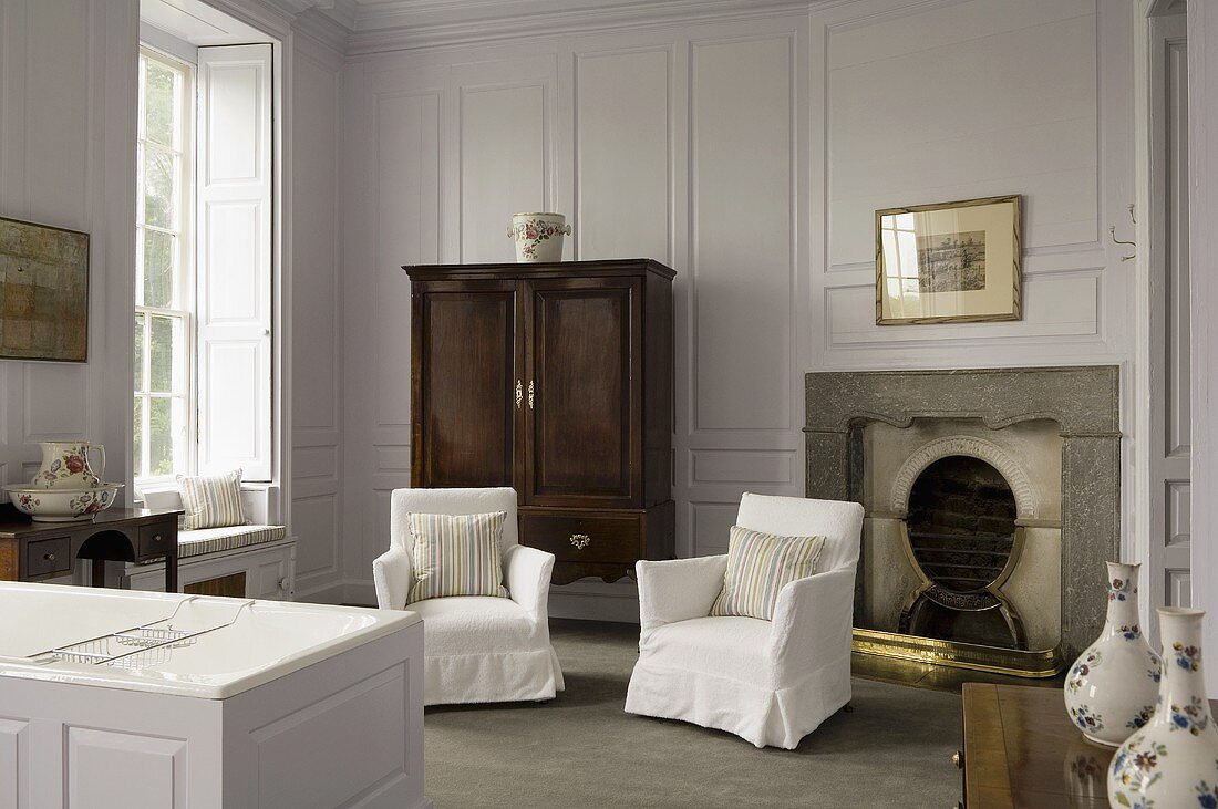 Bad im eleganten Landhausstil mit weissen Hussen Sesseln vor Kamin und fliederfarbenen Wänden