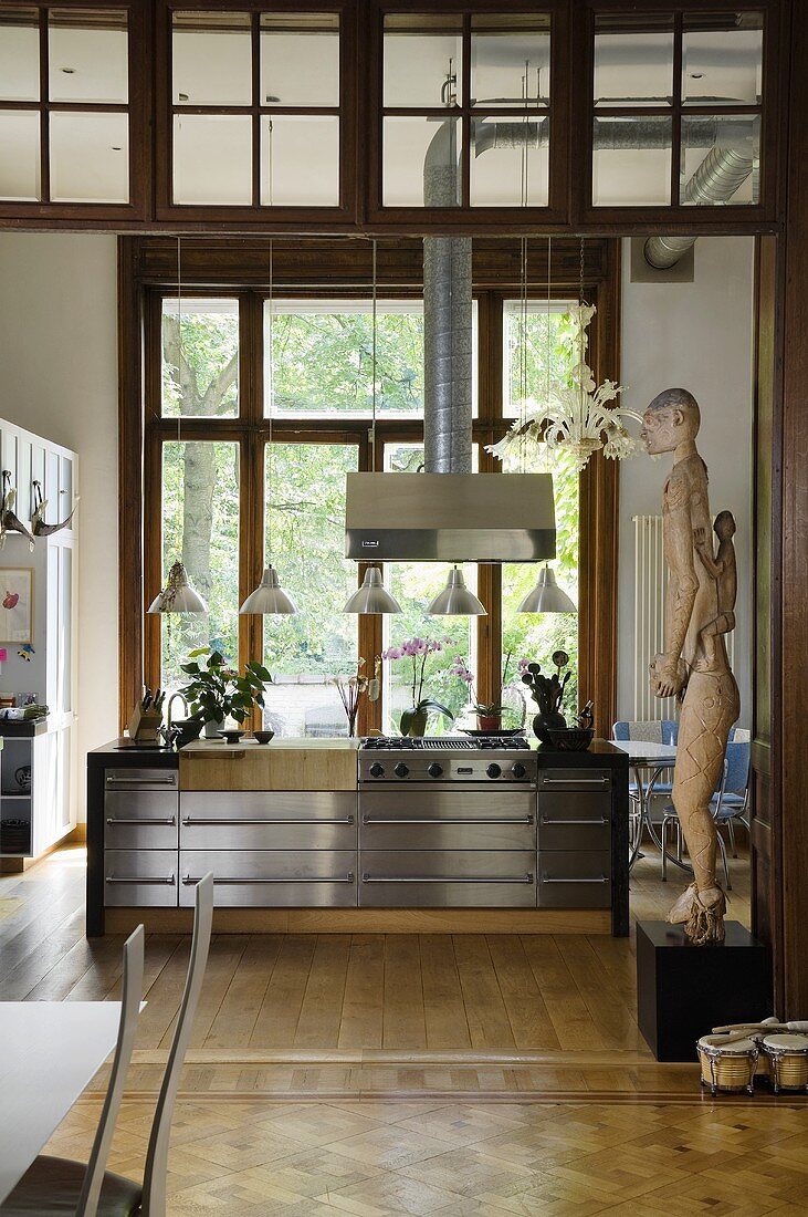 A view through a doorway onto a stainless steel kitchen island with an extractor fan positioned in front of terrace doors