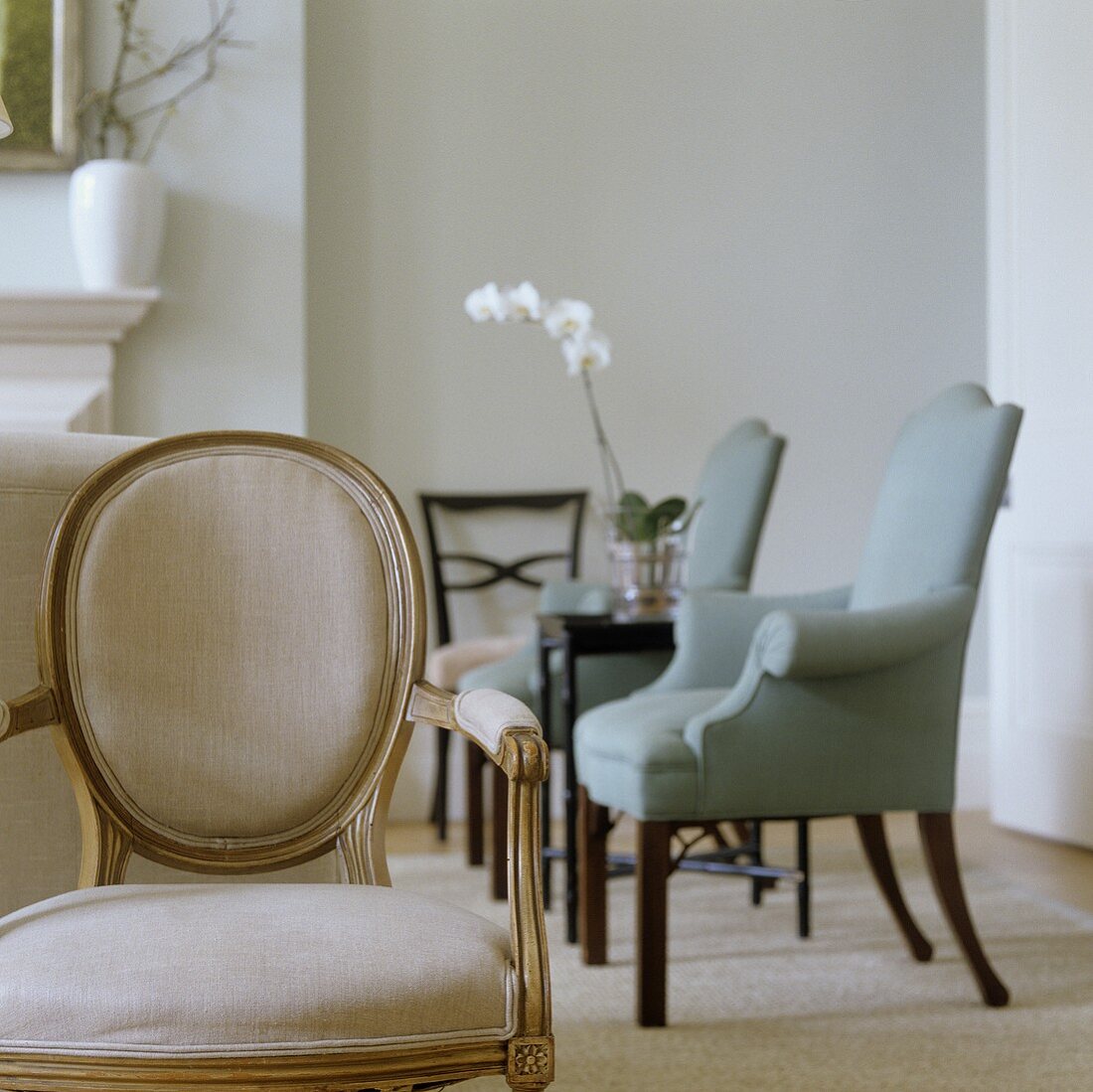 An antique upholstered chair with a light back and a view of upholstered armchairs