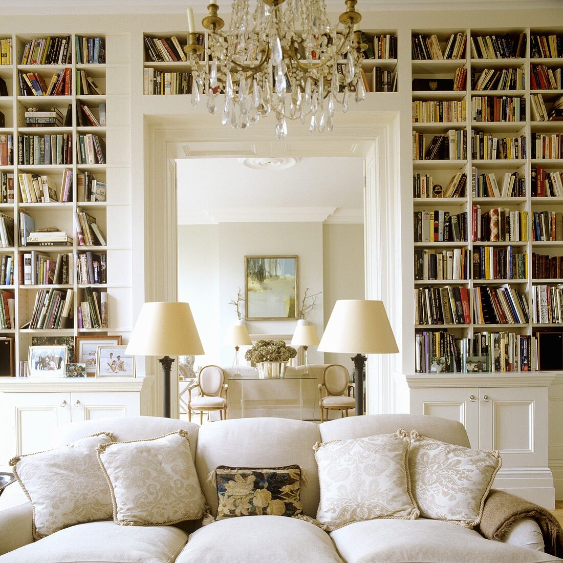 A light upholstered sofa in front of a built-in bookshelf with a view into a living room