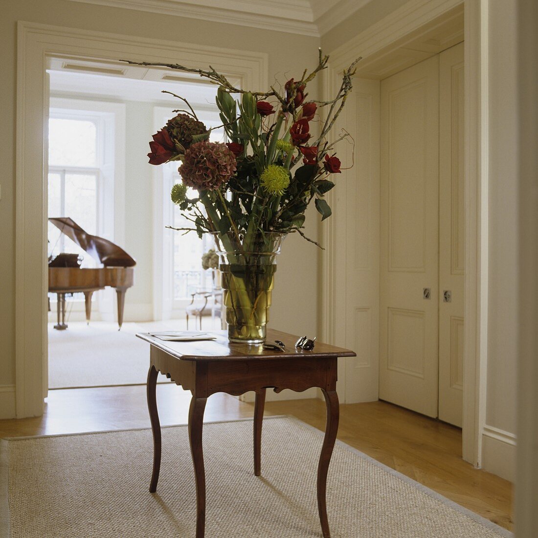 A large bunch of flowers on a Rococo-style occasional table with a view into a room with a piano