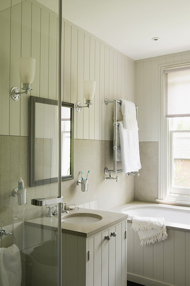 A wash basin and a mirror with wall lighting on a white wooden wall in a country-house style bathroom