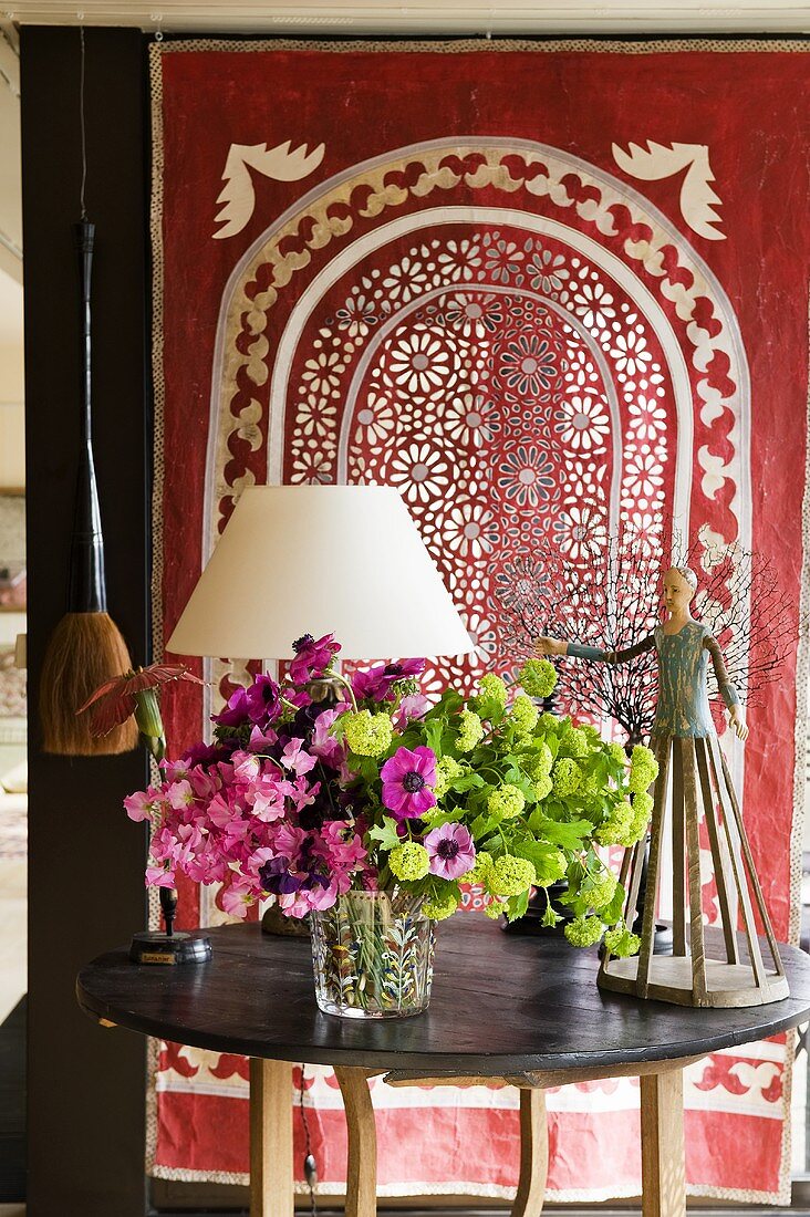 Flowers on a wooden table in front of a red ethnic cloth with a perforated pattern