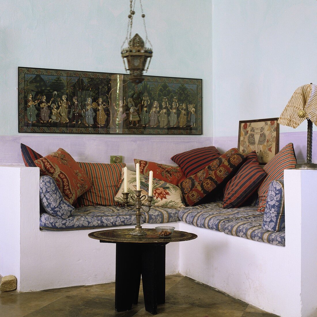 A Mediterranean-style living room corner - and occasional table with a metal tray and a candlestick in front of a concrete, upholstered pedestal with cushions