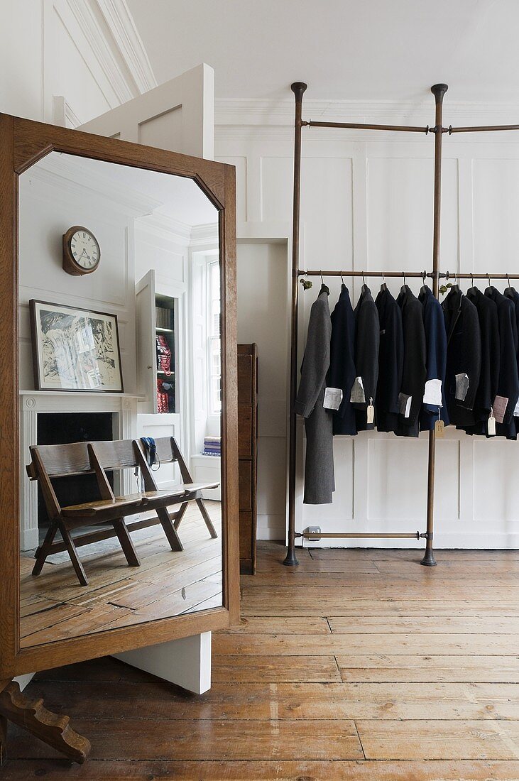 White wooden panelling in a living room - a studio with a tailor's mirror with a reflection and jackets hanging on a clothes rack