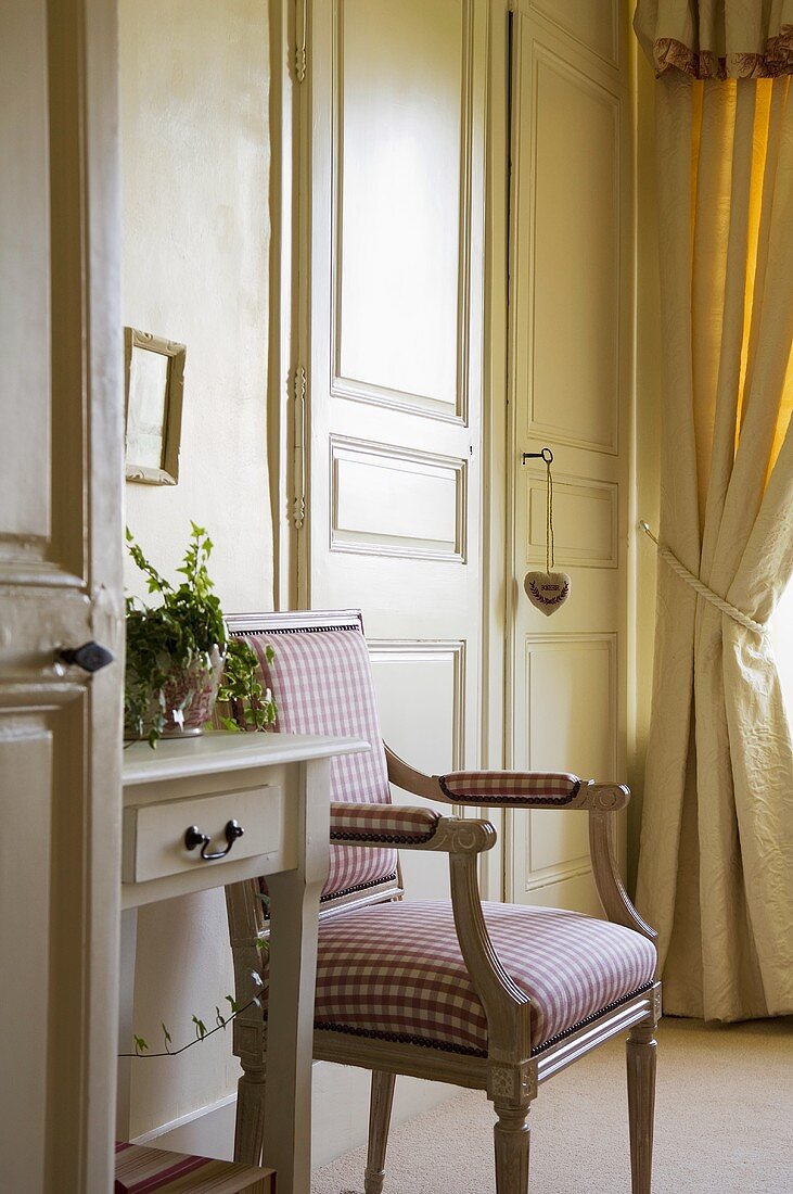 An upholstered chair with a red and white checked cover next to closed swing doors