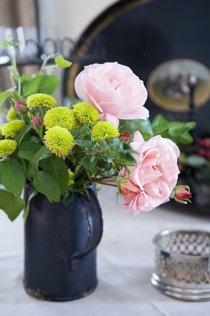 A bunch of flowers featuring pink roses in an old metal jug