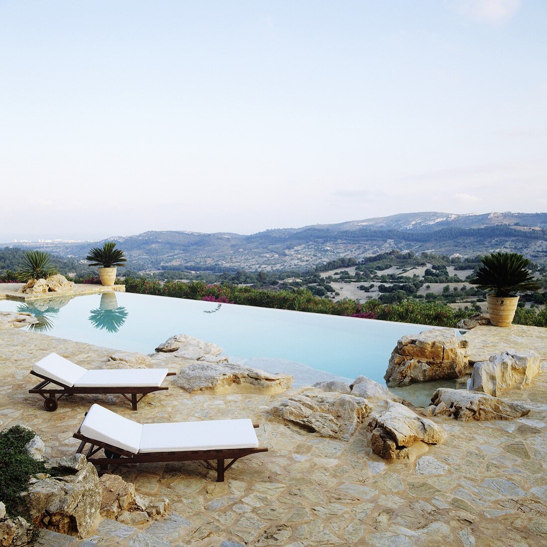 Liegestühle auf Natursteinboden vor Pool mit Ausblick auf die spanische Landschaft