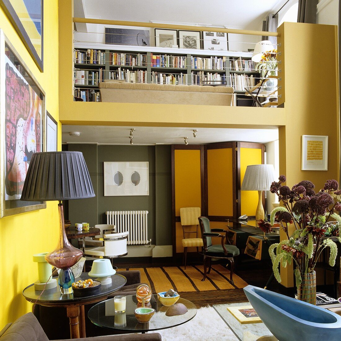 A maisonette apartment - living room with yellow walls and a view onto a gallery with a bookshelf