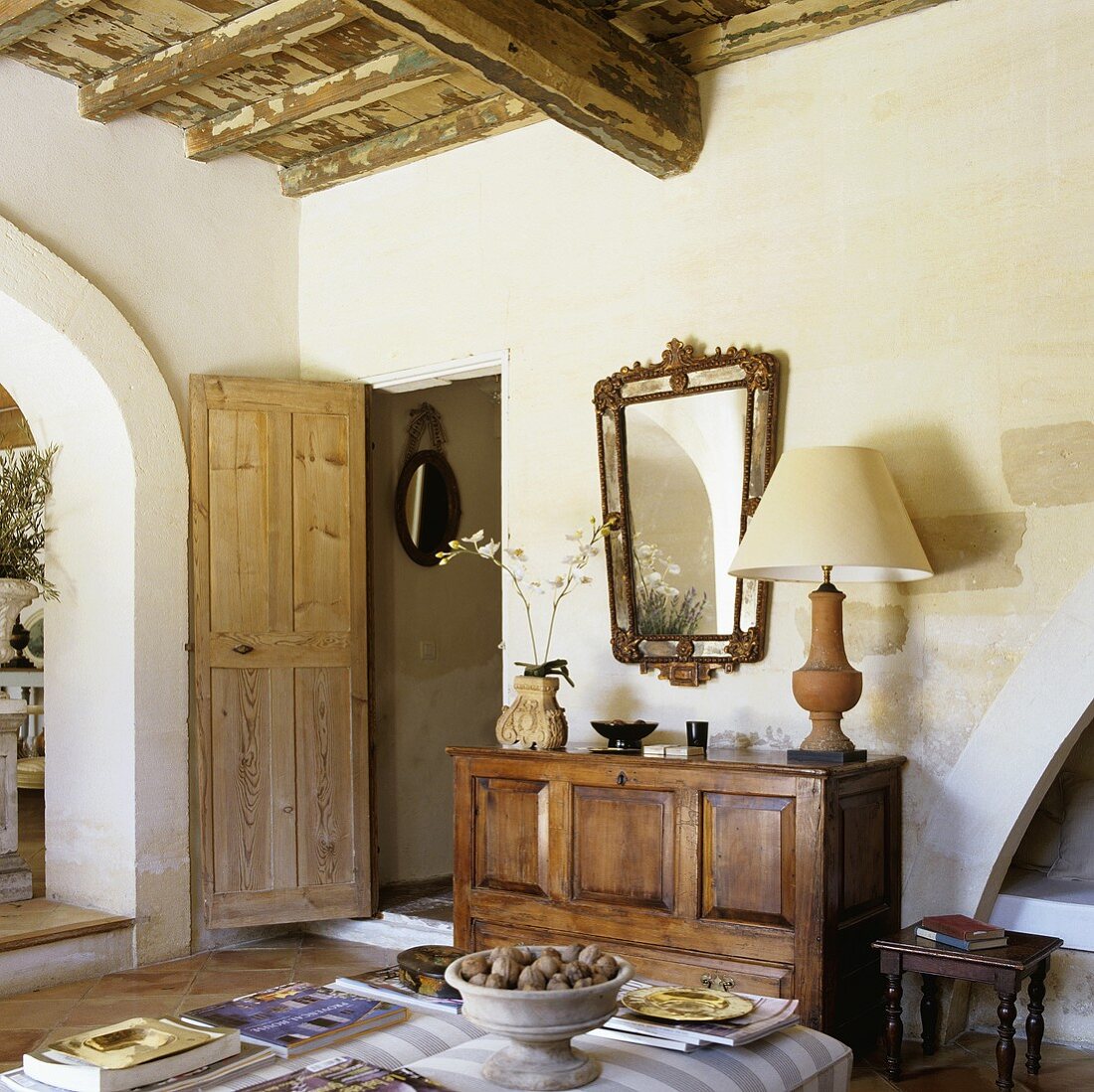 Living room in a Provencal style country home with rustic wooden ceiling and sideboard next to a wide open door