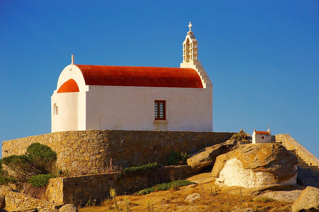 One of the hundreds of traditional red roofed chapels on Mykonos with a plane landing, Cyclades Islads, Greece