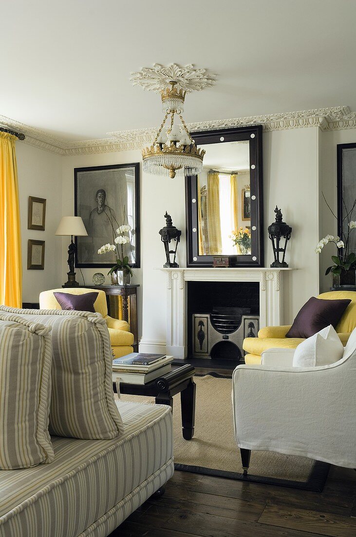 A living room with light upholstered furniture and a chandelier in front of a fireplace with a mirror hanging above it