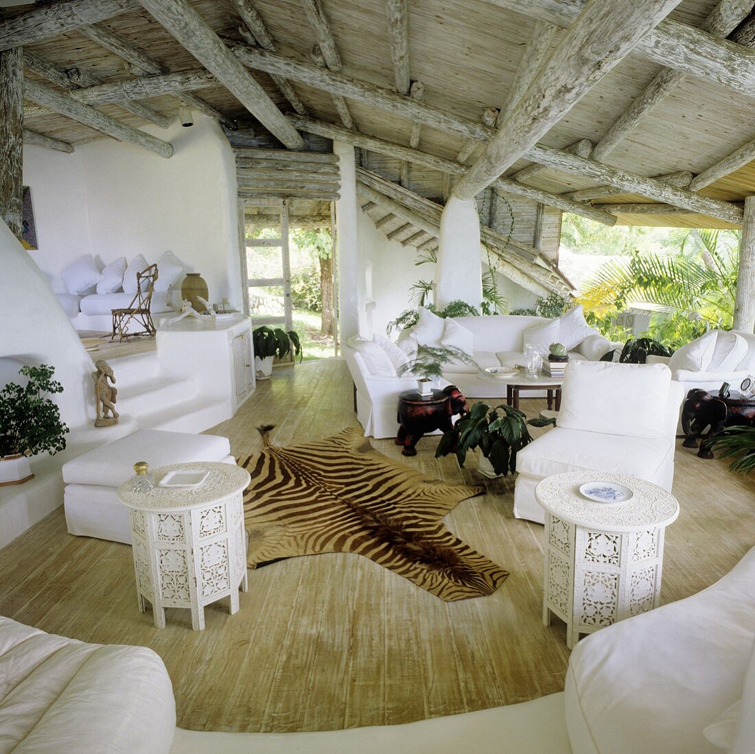 A rustic wood beam ceiling in a tropical one room house with an open view and an animal skin on the floor