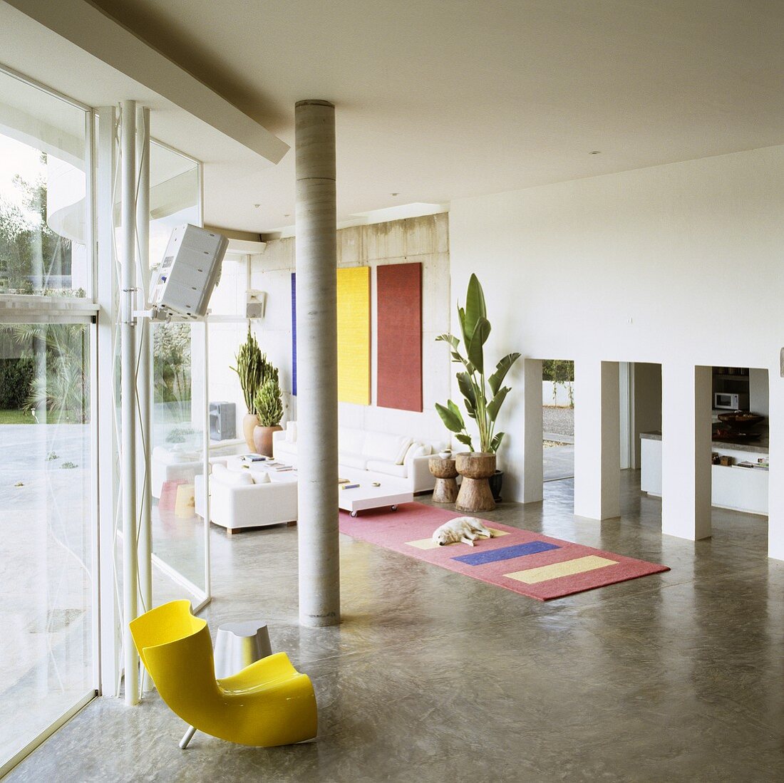 A Mediterranean house - a yellow plastic chair in front of a concrete pillar and a view through a row of arches into an open-plan living room