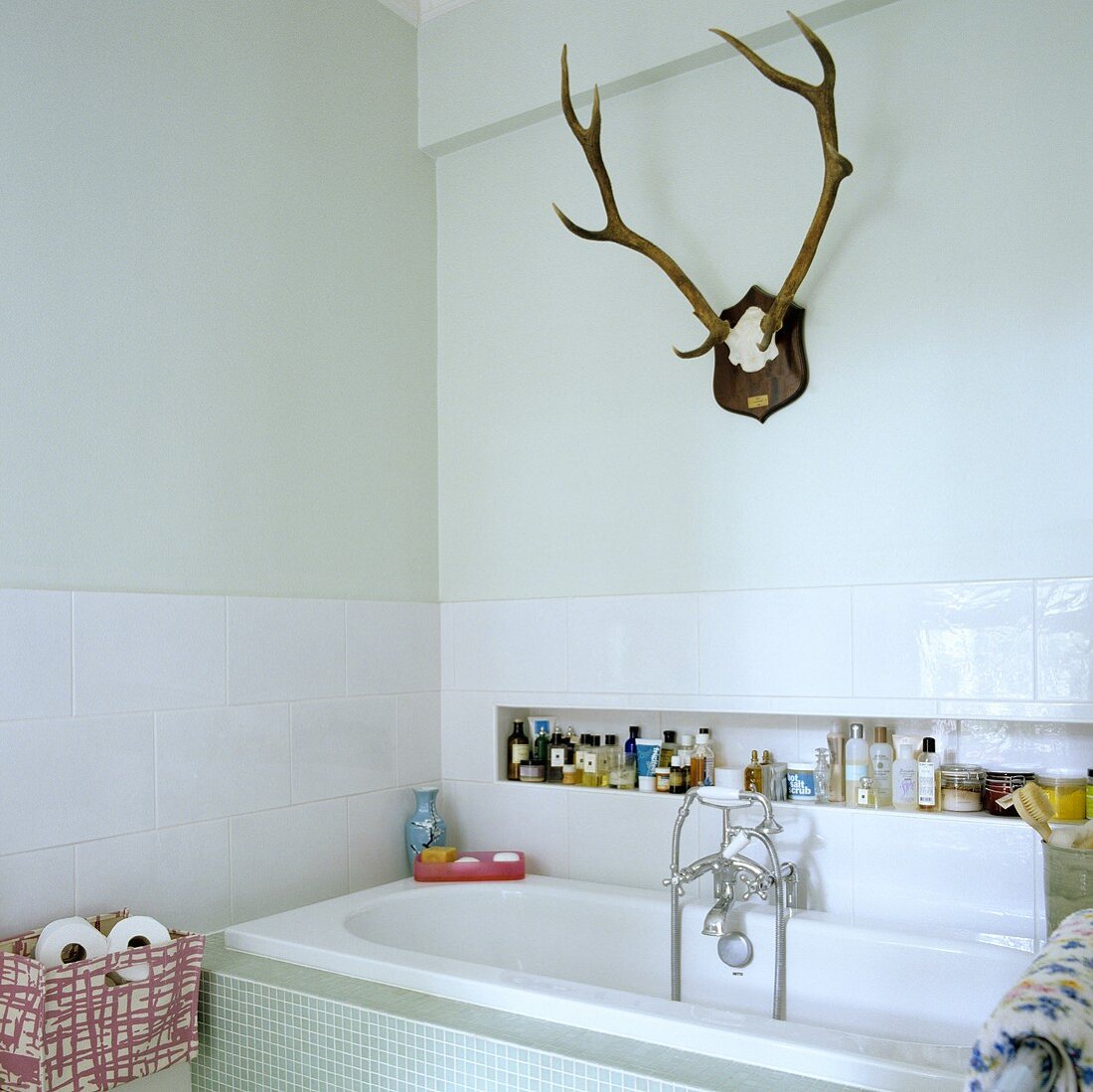 Antlers in a white bathroom with bathtub and bathing products in a niche