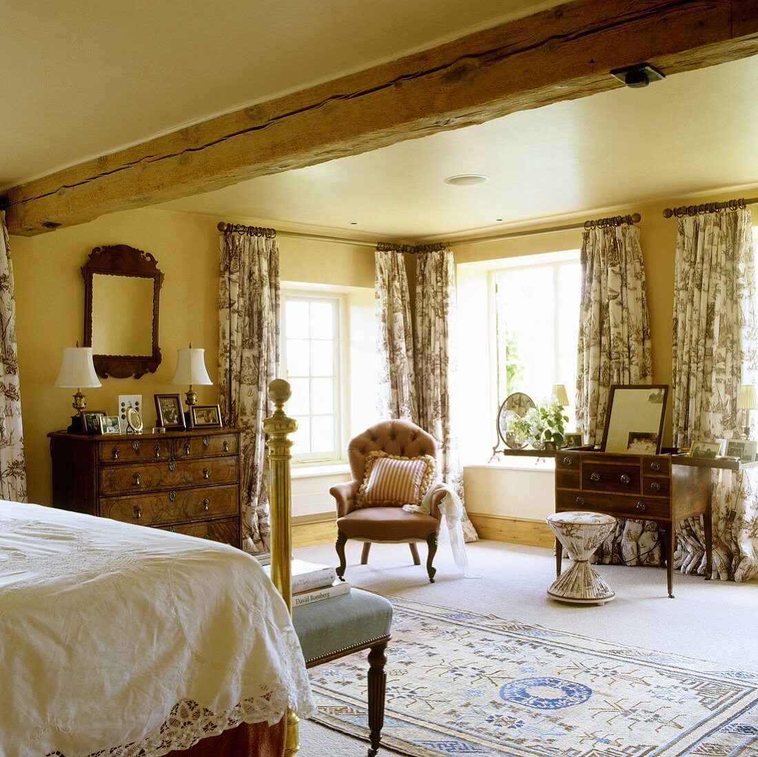 A yellow-painted bedroom in an old country house with antique furniture and floor-length patterned curtains