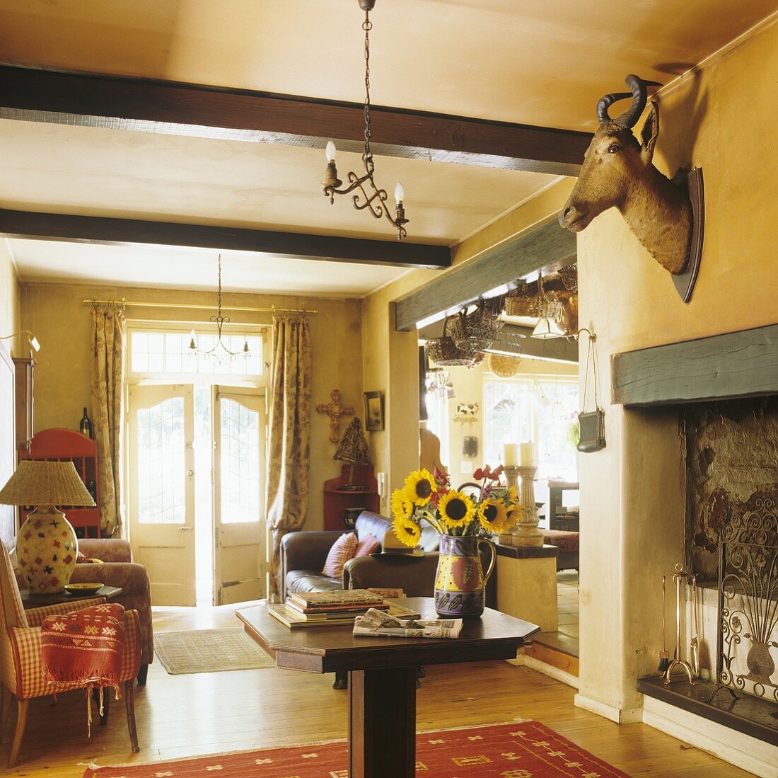 A yellow living room with a wood beam ceiling and a stuffed animal head on the wall above the fireplace