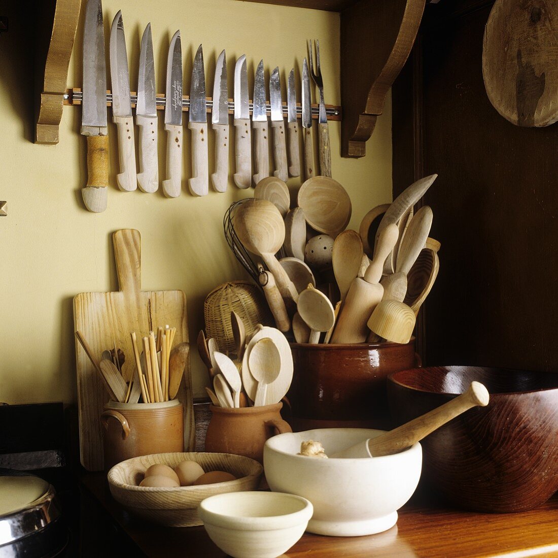 Kitchen implements in container and an assortment of knives on the wall