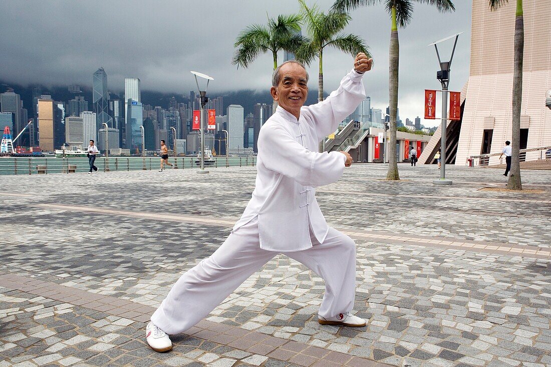 Portrait of Tai Chi master Mr  Ng at a shadow boxing posture shoot at the Avenue of Stars with Hong Kong?s skyscrapers noticeable at the background , Kowloon, Hong Kong, China, Asia