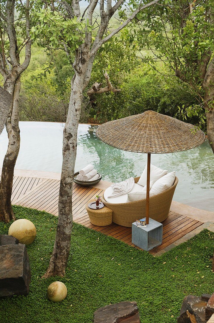 South Africa - bamboo shades and wicker chairs on a wooden terrace by a pool in a garden