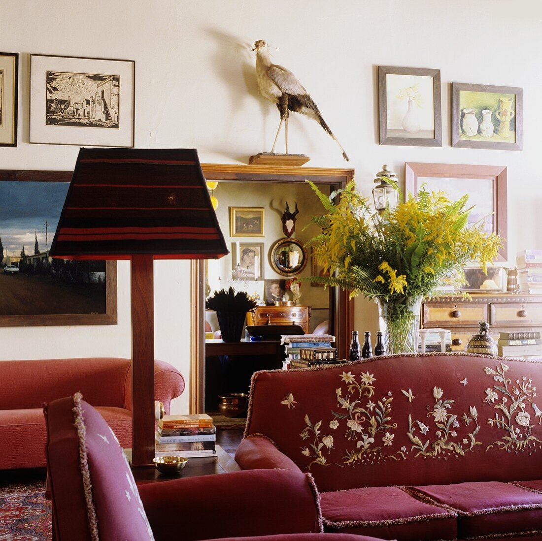 A red sofa with an embroidered back and a table lamp with a striped shade in a South African country house