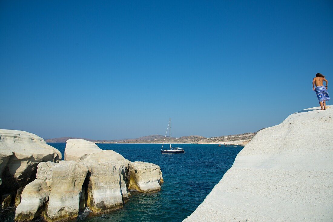 woman and sailboat at the white sandstone cliffs of Sarakiniko beach at Milos in Greece