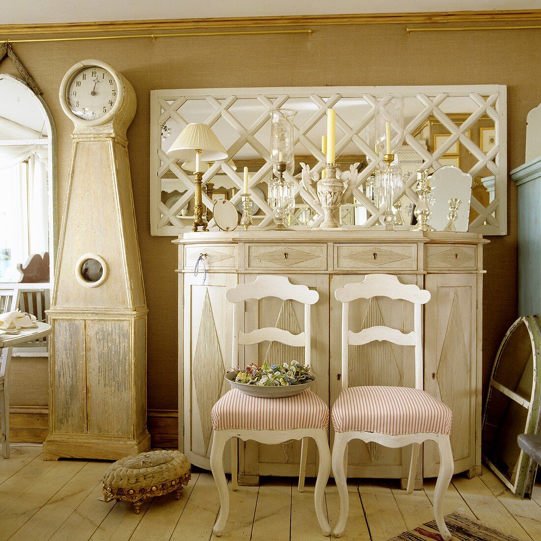 Candlesticks on a light wooden sideboard in an anteroom with two white country house-style chairs in front of it