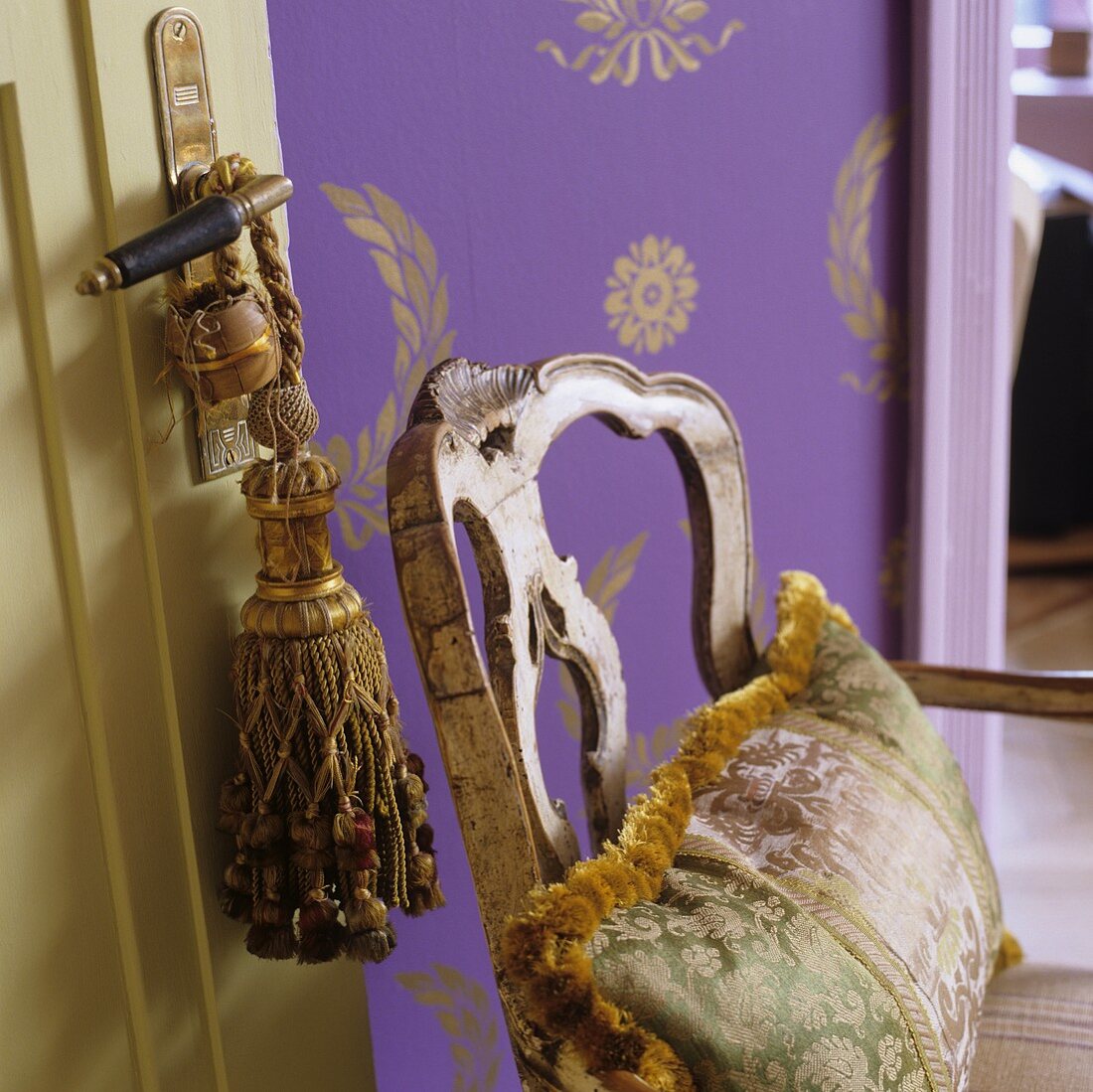 Silk pillows on a vintage wooden chair in front of purple wallpaper with gold colored Oriental pattern