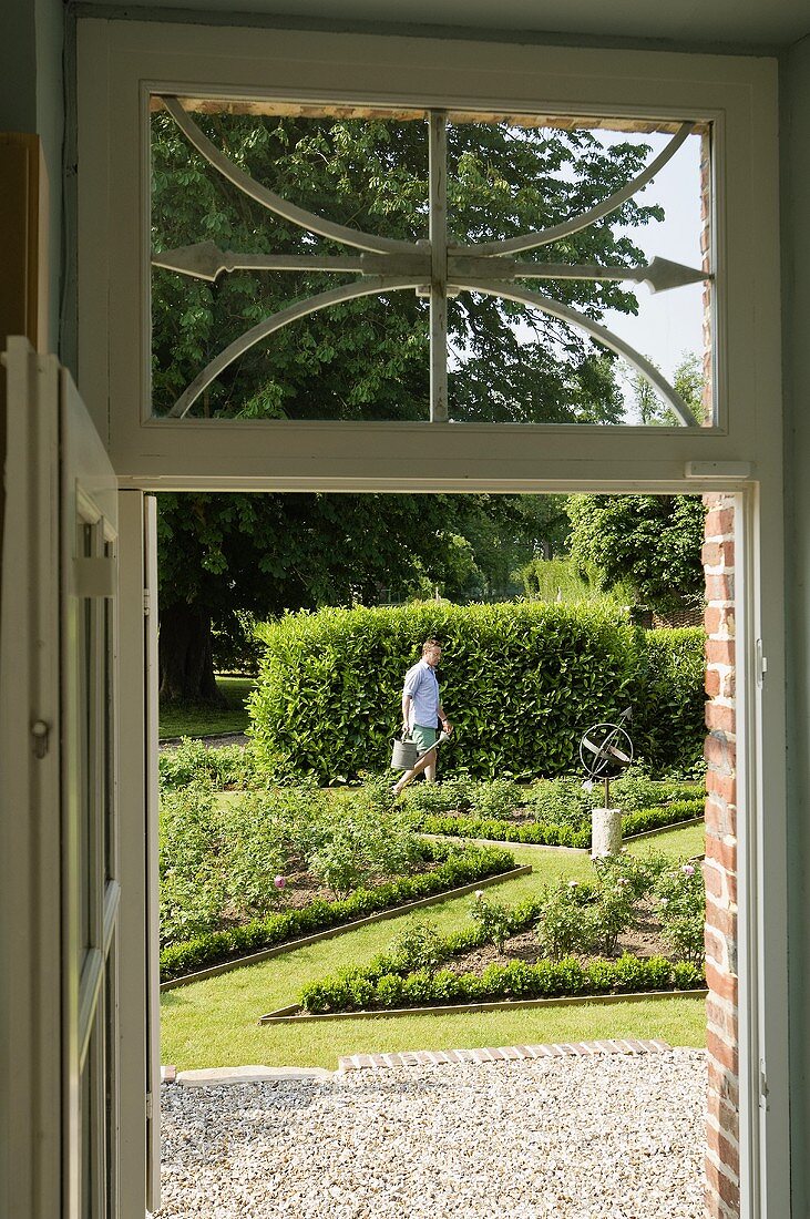 A view through a door into a garden and a gardener tending borders