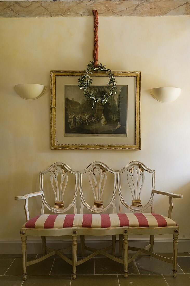 An antique, white-painted bench with a red and white striped cover in a hallway