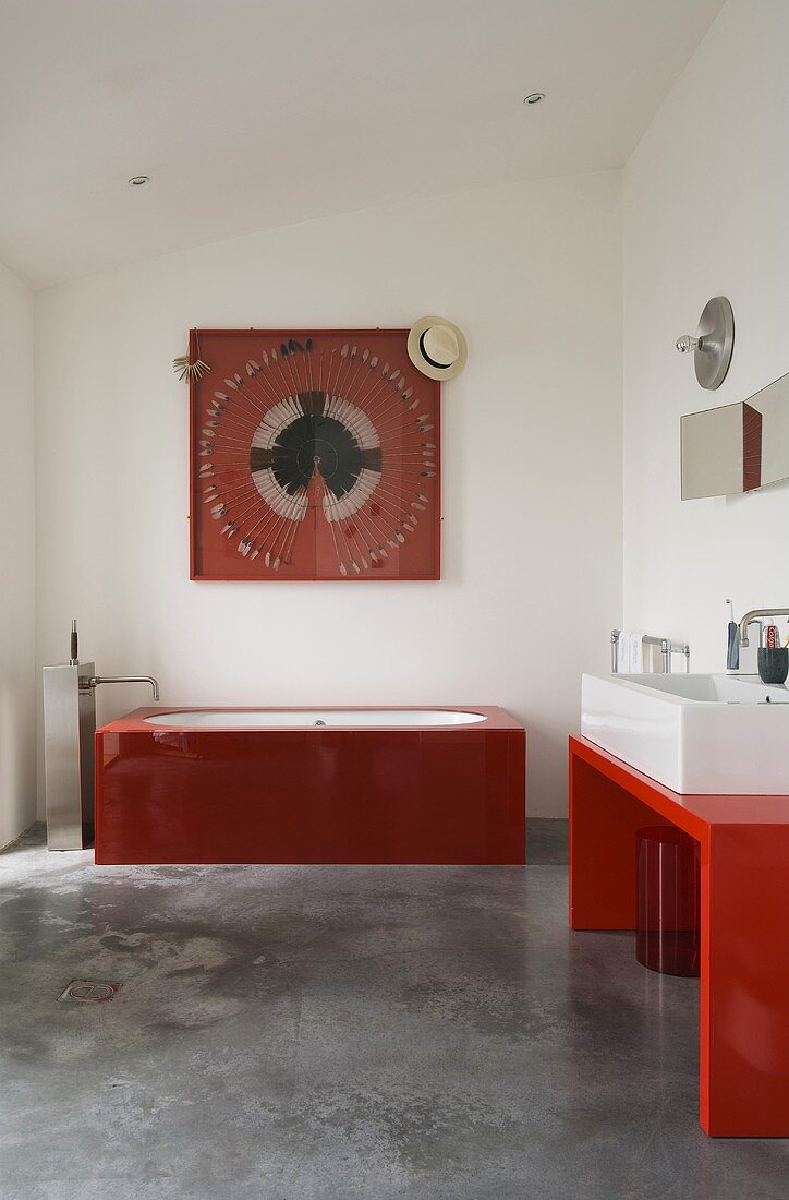 A red glass bathtub in a minimalistic white-painted bathroom with a grey concrete floor