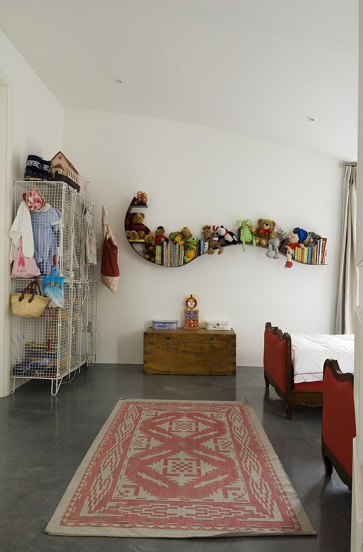 A child's bedroom with a long rug in front of a toy box and a curved wall shelf