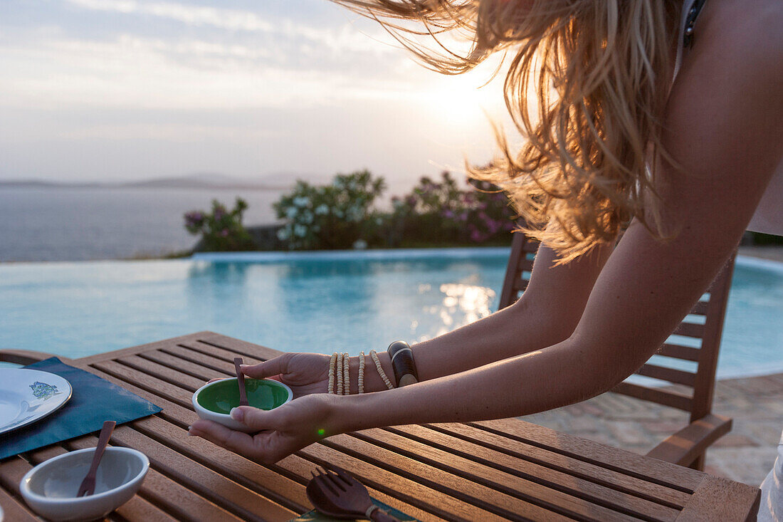 Junge Frau deckt Gartentisch an einem Pool, Mykonos, Griechenland