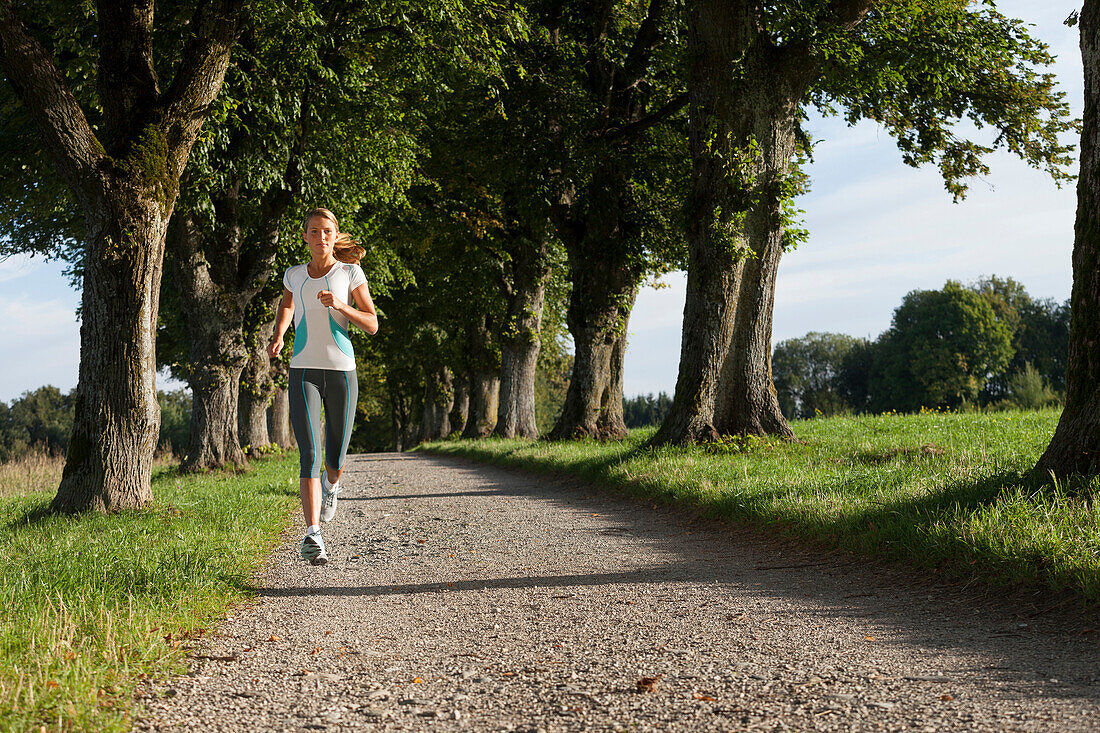 Young woman jogging, alley near Aufkirchen, Berg, Bavaria, Germany