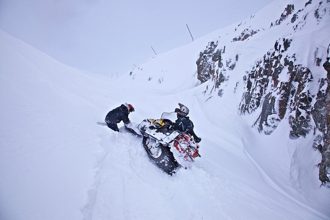 zwei Männer beim Ausgraben eines, im Tiefschnee steckengebliebenen, Schneemobils, Tschukotka (Autonomer Kreis der Tschuktschen), Sibirien, Russland