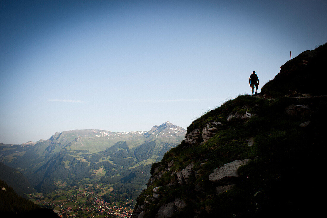 Hiker on mountain trail, on the way to Schreckhorn hut, at the bottom left the village of Grindelwald, Bernese Oberland, Switzerland