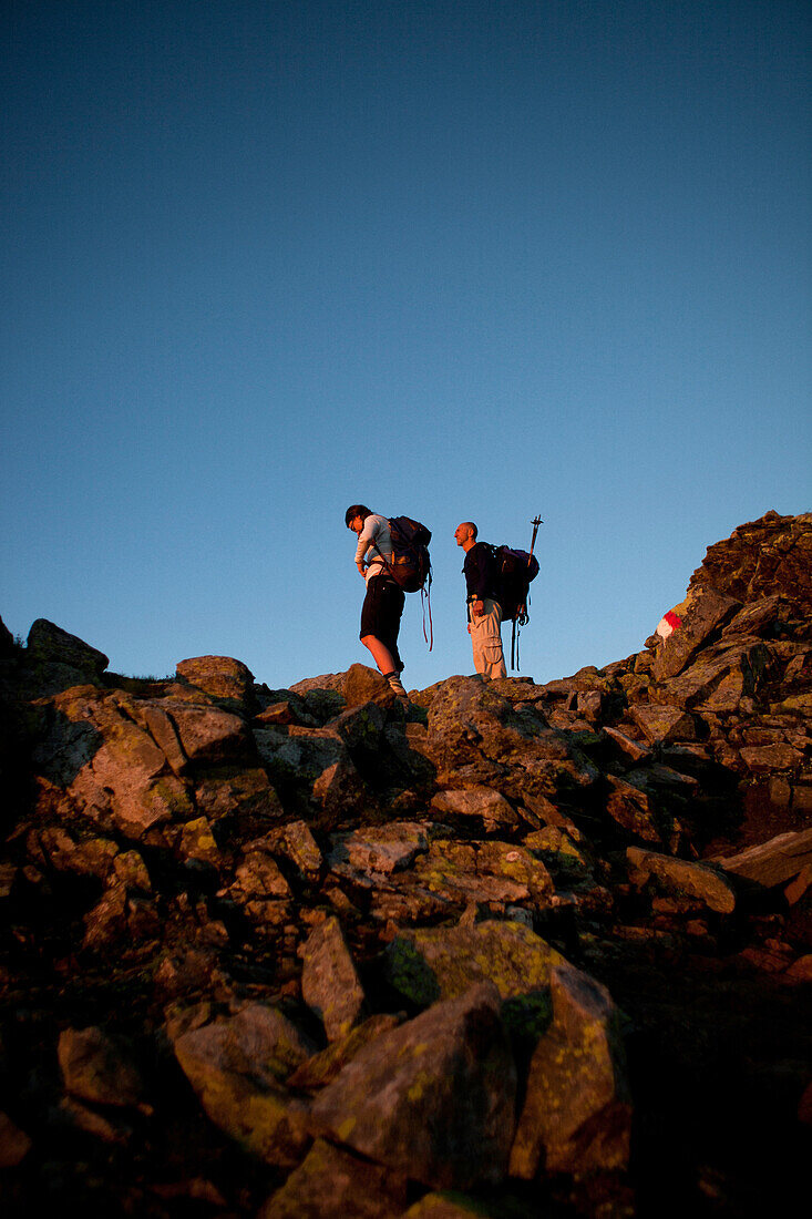 Hikers in rocks observing the sunrise, ascend to Habicht (3277 m), Stubai Alps, Tyrol, Austria