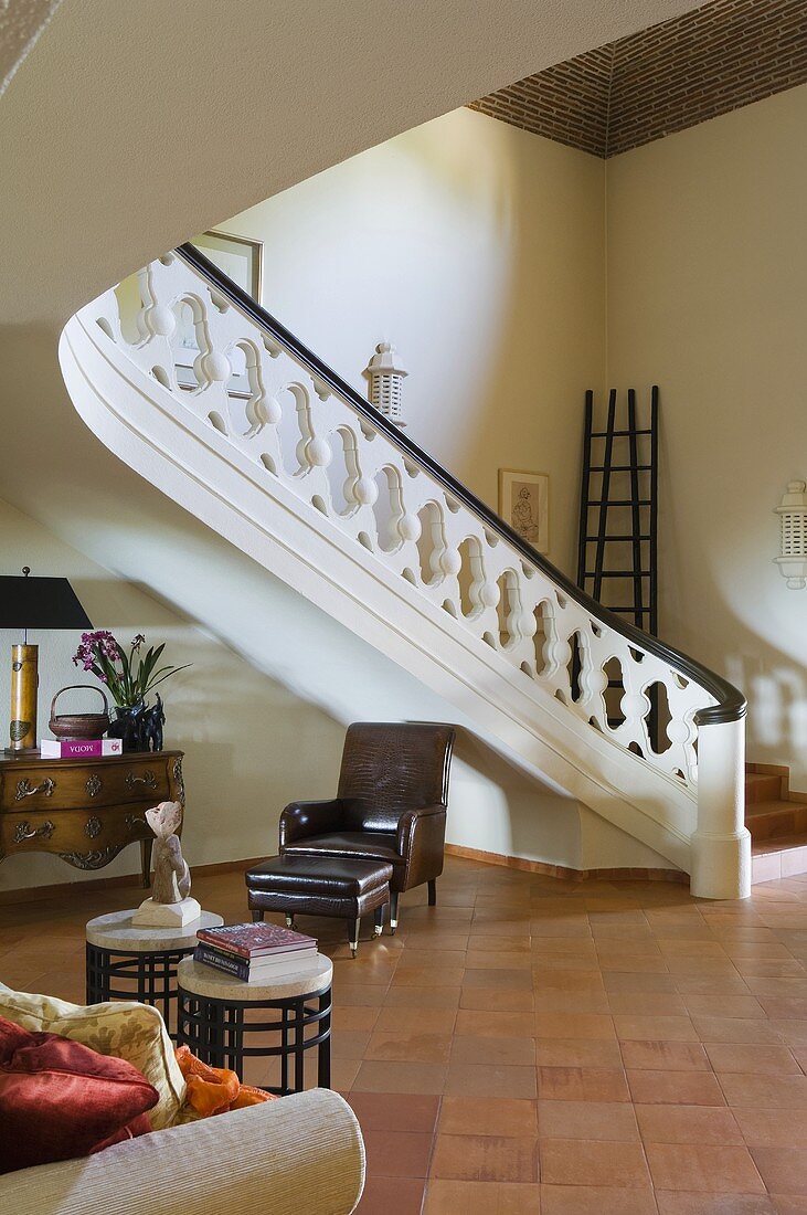 A hotel lobby - a flight of stairs with a balustrade, a leather armchair and a terracotta floor