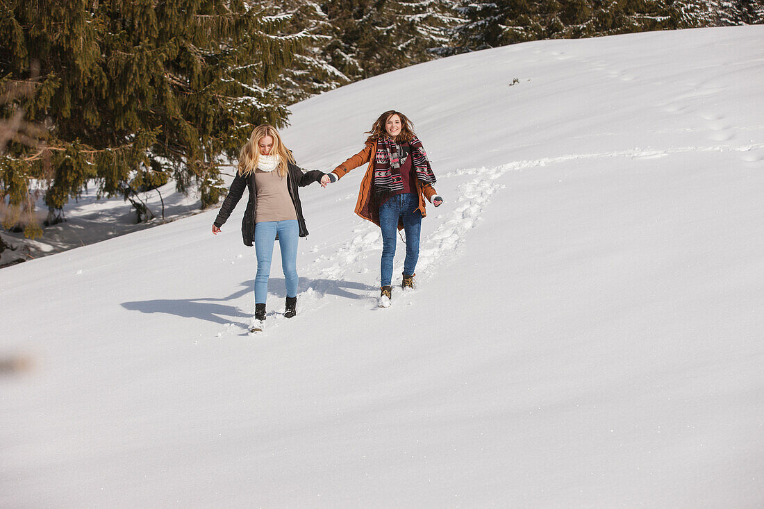 Two young women walking hand in hand in snow, Spitzingsee, Upper Bavaria, Germany
