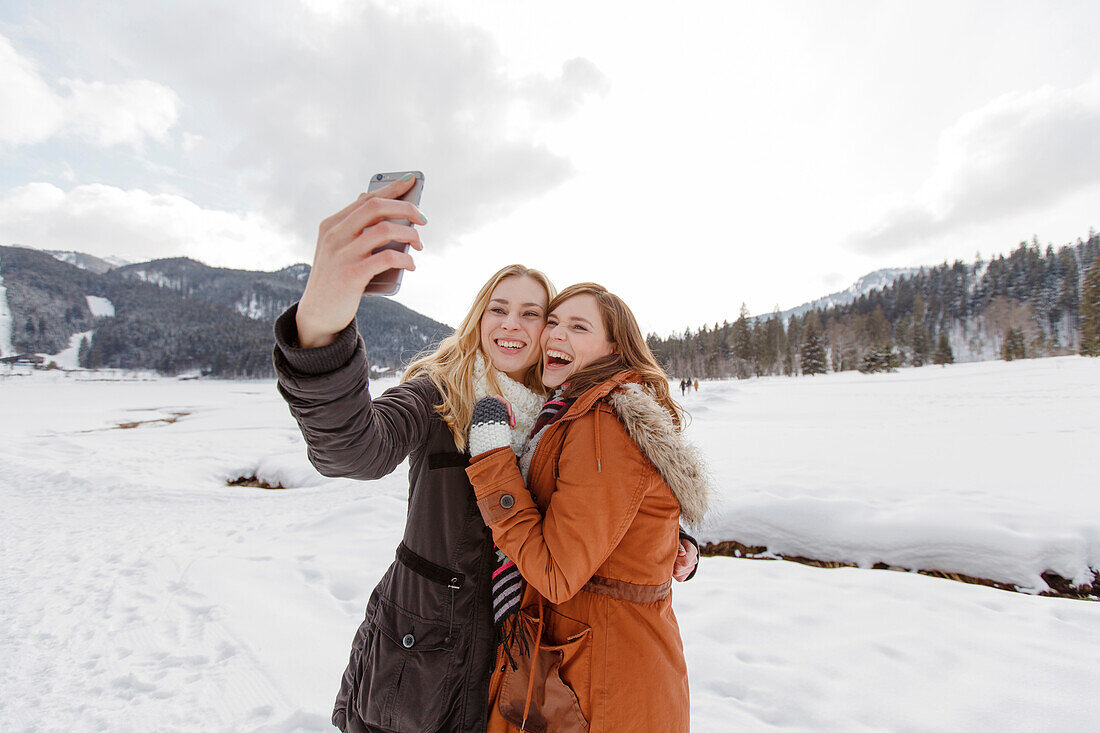 Two young women taking a selfie picture, Spitzingsee, Upper Bavaria, Germany