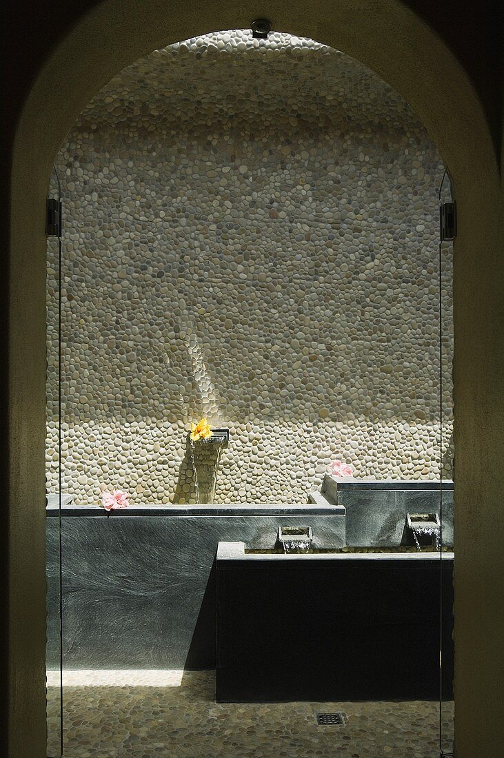 A view through an arched doorway onto a spa pool against a natural stone wall