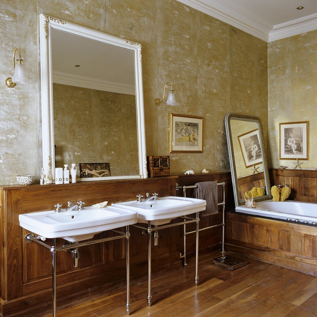 An antique bathroom with two wash basins and a mirror hung on a gold-painted wall above wood panelling
