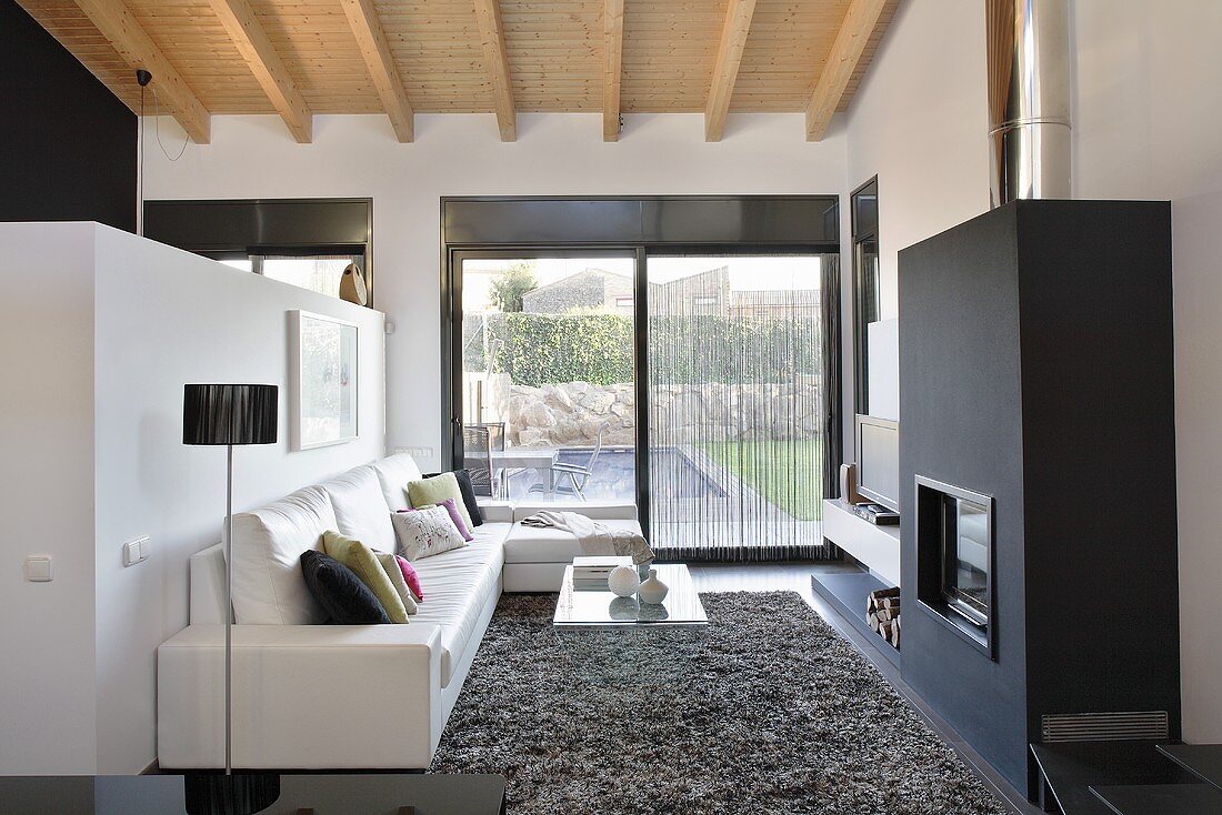 A designer living room with a view of the garden - a leather sofa in front of a partition wall in front of a black fireplace