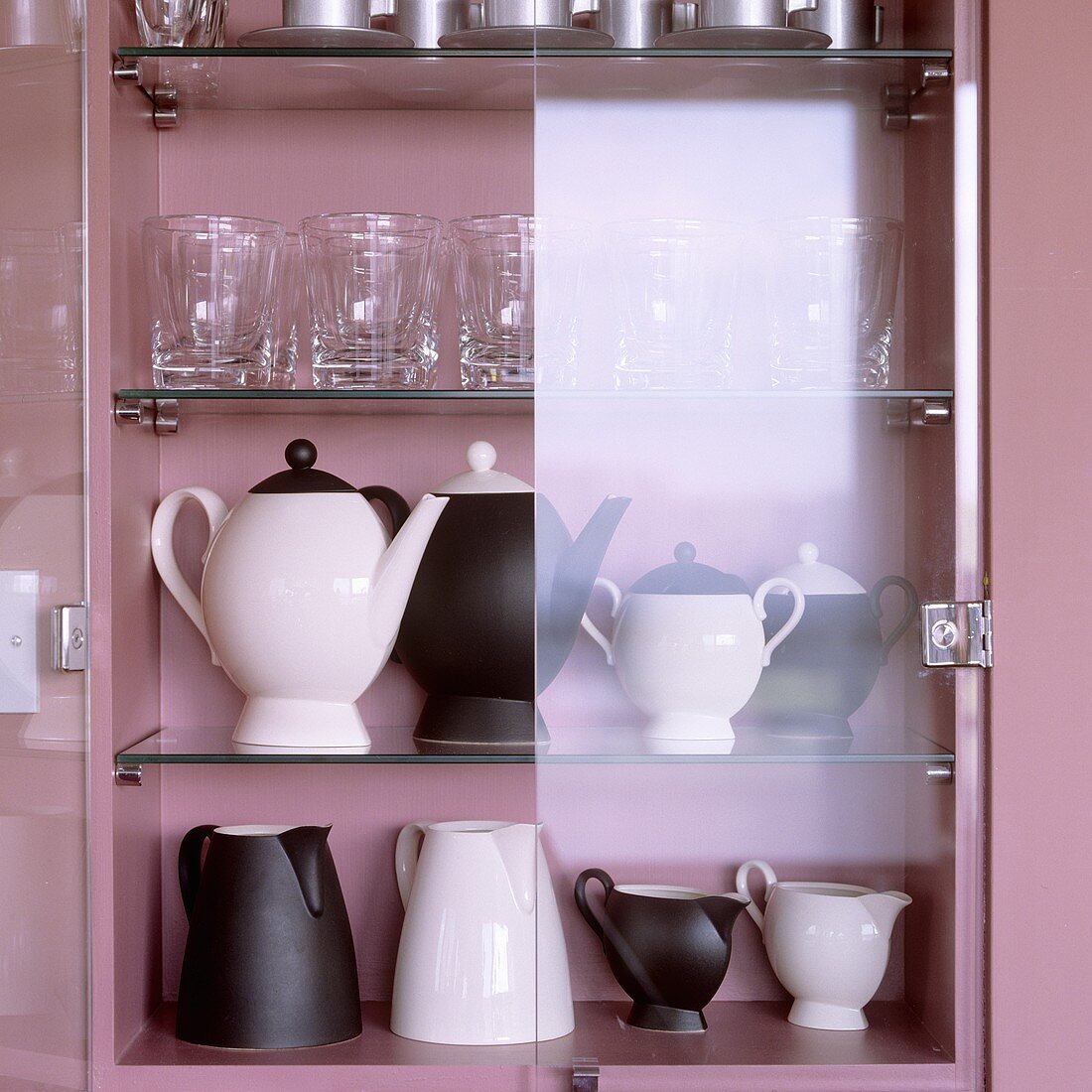 Schwarzweisse Kannen und Gläser im rosalackierten Schrank mit offener Glastür