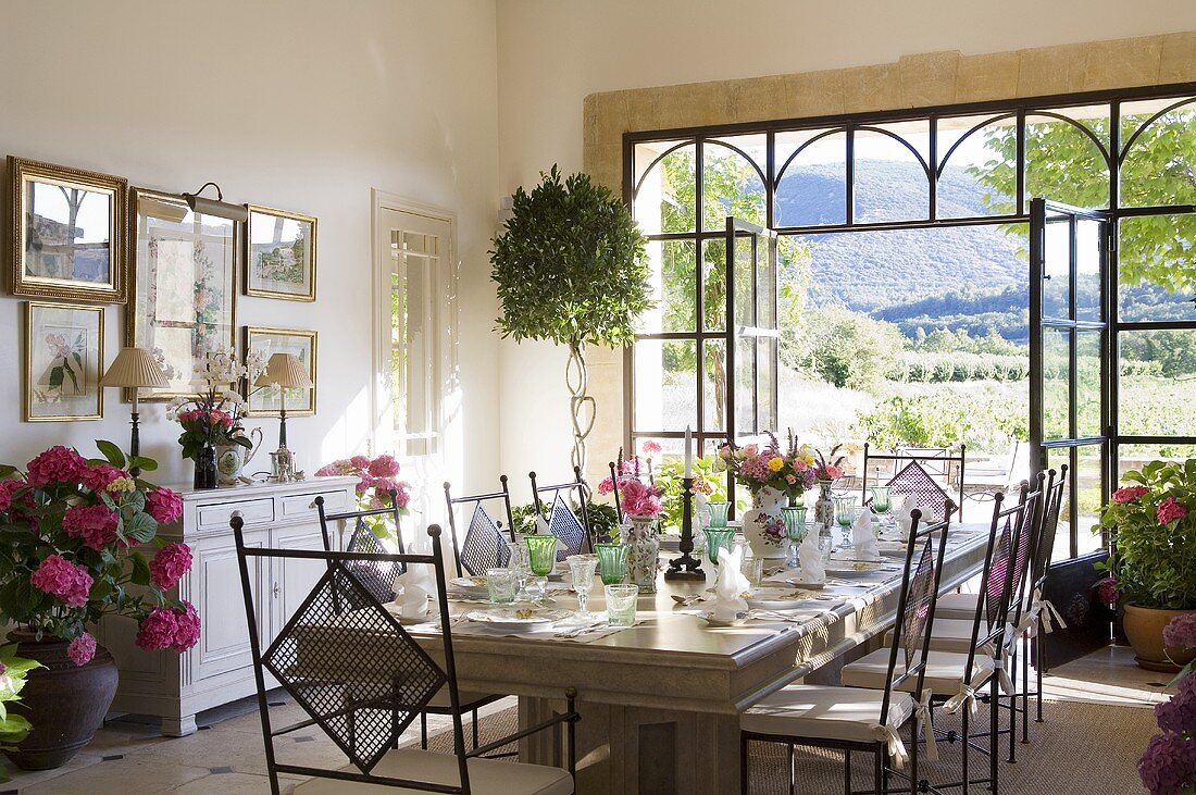 Mediterraner Esszimmer mit Festtafel vor geöffneten Terrassentüren mit Aussicht