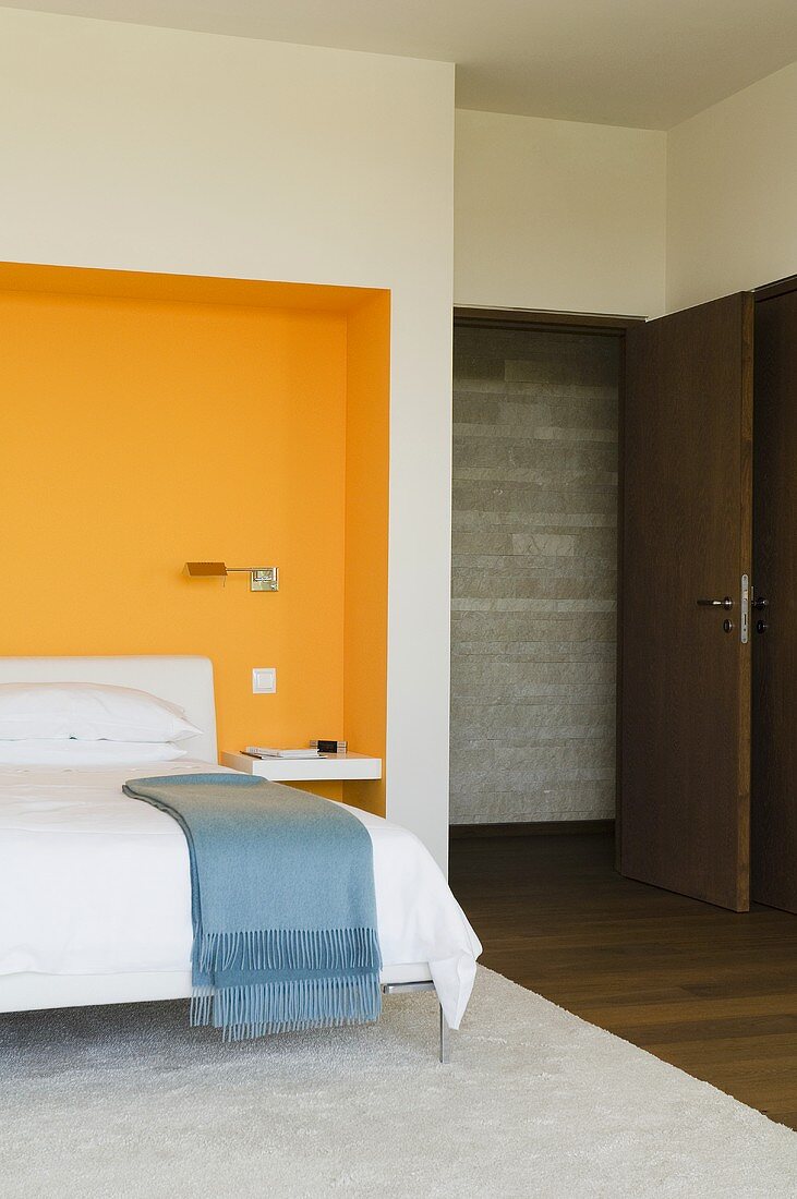A bedroom with a bed in an orange-painted wall niche and an open door