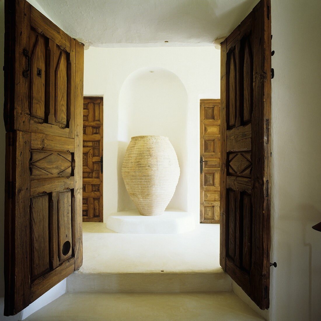 A view through open double door onto a an amphora in a wall niche in a Mediterranean house